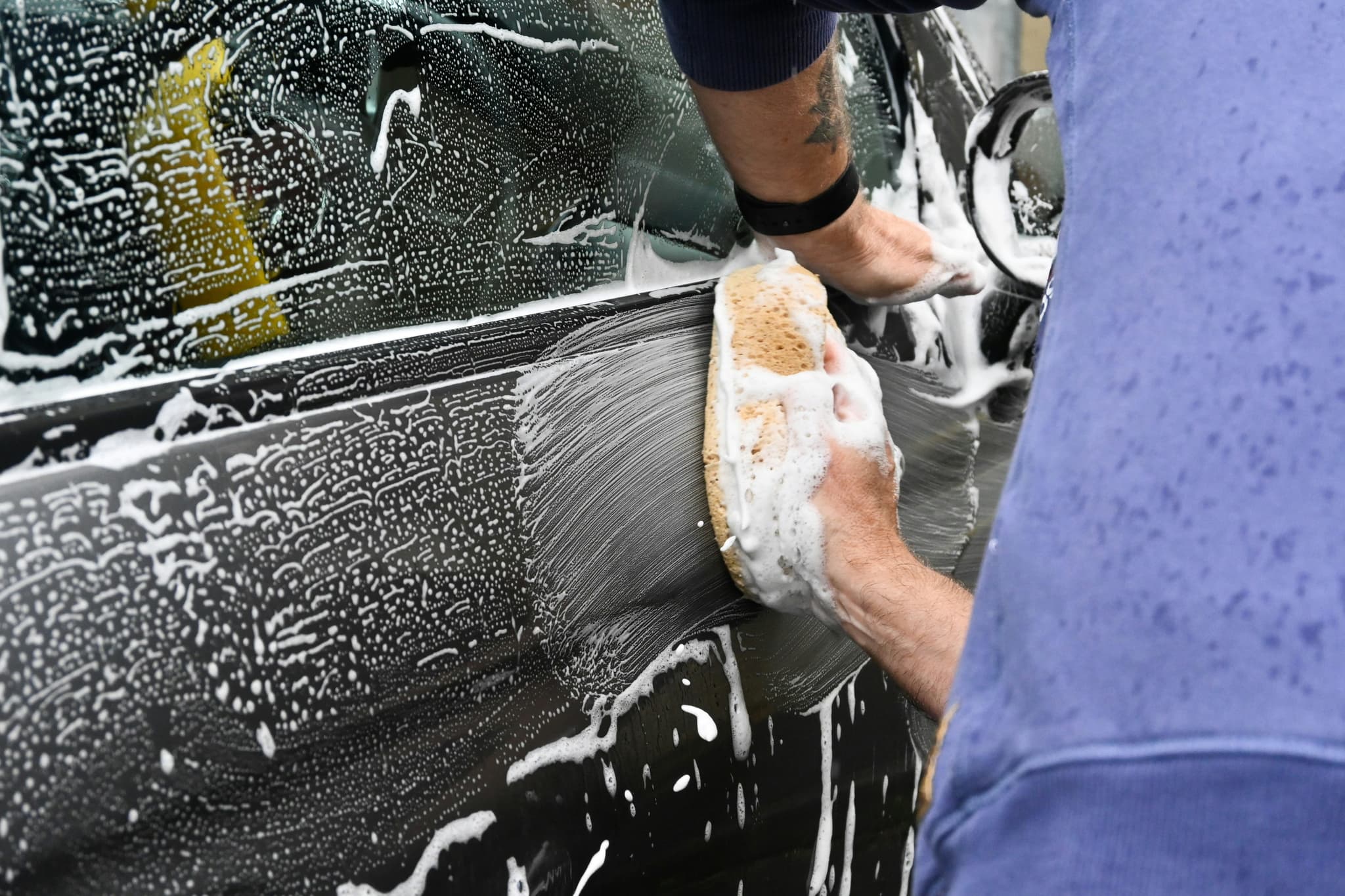 Hands washing a black car with a soapy sponge