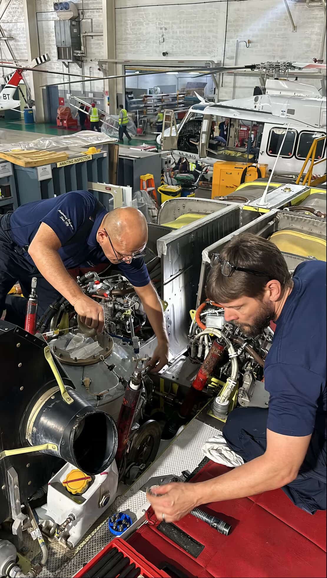 Two technicians working on an aircraft component together on the hangar floor.